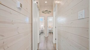 A narrow hallway with wooden walls and a wooden floor, leading to a room with a bed and a nightstand. - Save The Ales~Boardwalk~Private Pool~Sleeps 10! (Port Aransas)