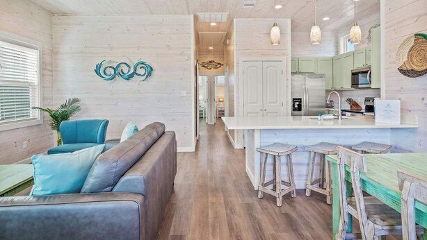 A modern kitchen with white cabinets, a central island with stools, and pendant lighting. - Save The Ales~Boardwalk~Private Pool~Sleeps 10! (Port Aransas)
