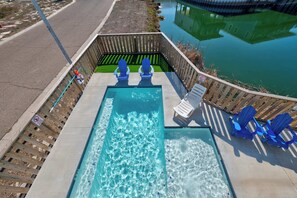 A rectangular pool with two blue Adirondack chairs and a wooden deck.