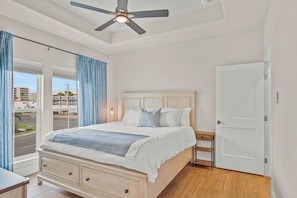 Une chambre à coucher avec un lit, un ventilateur de plafond, une table de chevet, une porte et une fenêtre avec des rideaux.