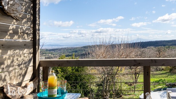 Eine Holzterrasse mit einem Tisch, auf dem eine Flasche und Gläser stehen, mit Blick auf eine malerische Landschaft.