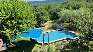 Ein Schwimmbecken, umgeben von einem Holenzaun, mit Blick auf ein bewaldetes Gebiet und einen entfernten Berg.