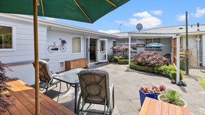 A patio area with a wooden table and chairs, a green umbrella, and a small garden with potted plants. - Hidden Gem (Hamilton)