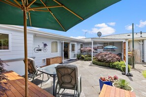 A patio area with a wooden table and chairs, a green umbrella, and a small garden with potted plants. - Hidden Gem (Hamilton)