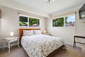 A bedroom with a large bed, two bedside tables, a wooden headboard, and two windows with curtains. - Hidden Gem (Hamilton)