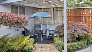 A patio with a table and chairs, a striped umbrella, and a wooden fence.