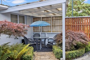 A patio with a table and chairs, a striped umbrella, and a wooden fence. - Hidden Gem (Hamilton)