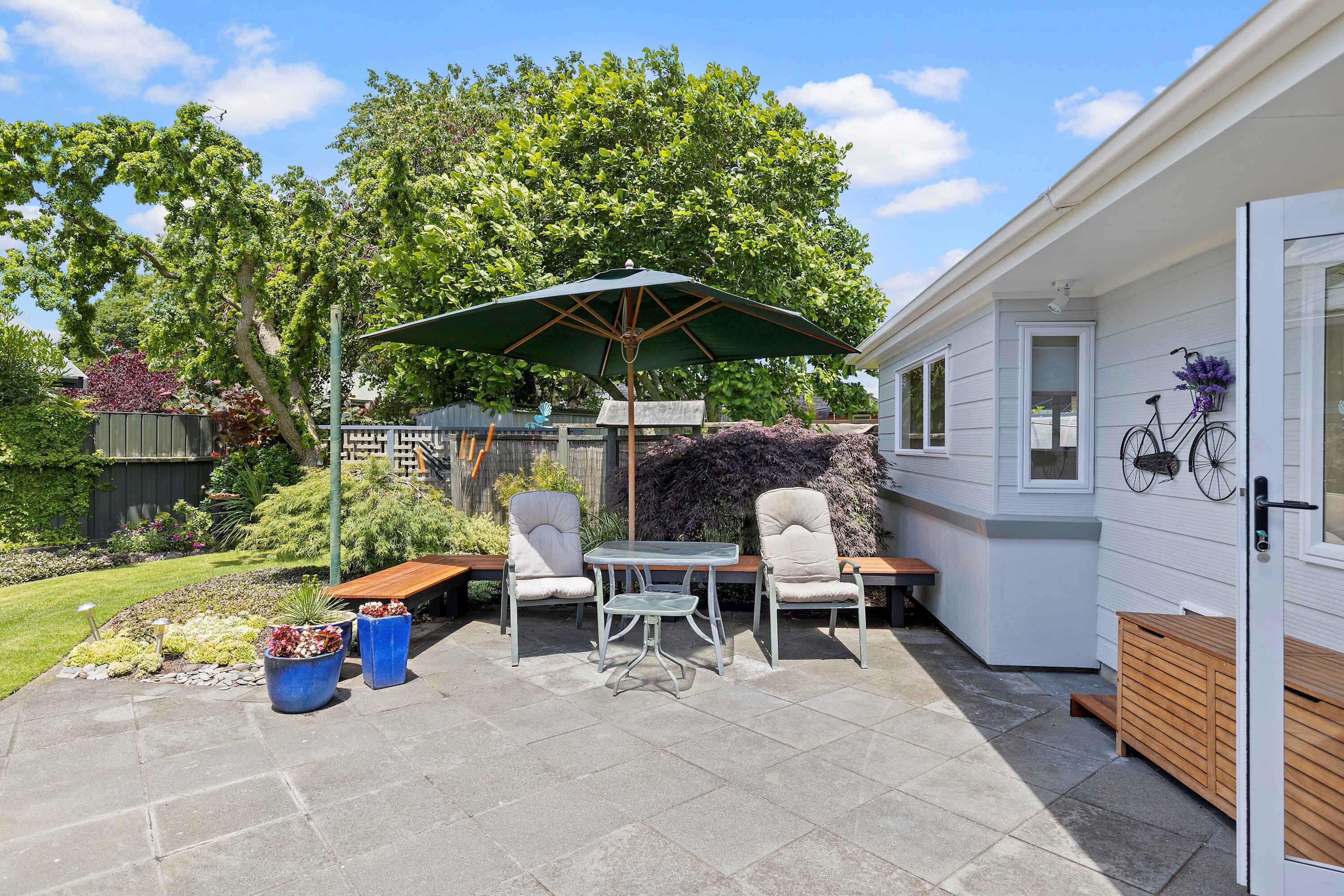 A patio with a table and chairs, a wooden bench, and a green umbrella.