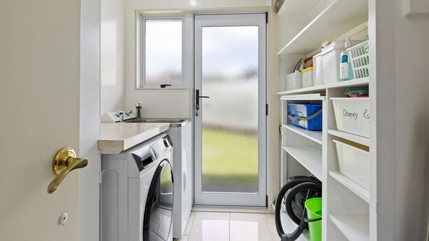 A compact laundry room with a washing machine, a dryer, a small sink, and a door with frosted glass panels. - Hidden Gem (Hamilton)