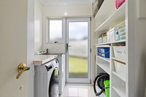 A compact laundry room with a washing machine, a dryer, a small sink, and a door with frosted glass panels. - Hidden Gem (Hamilton)