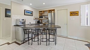 A modern kitchen with a central island, bar stools, a stainless steel refrigerator, and a microwave.