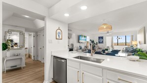 A modern kitchen with white cabinetry, a built-in dishwasher, and a large island with a sink. - Bay & Sunset Views I 6-Seat Golf Cart I Sleeps 8 (Miramar Beach)