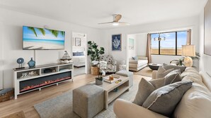 A living room with a fireplace, a television, a sofa, and a large window. - Bay & Sunset Views I 6-Seat Golf Cart I Sleeps 8 (Miramar Beach)