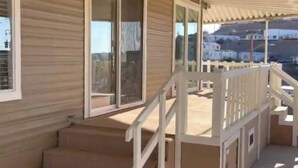 Un balcón cubierto con barandilla blanca, ventanas grandes y vista a una zona residencial.