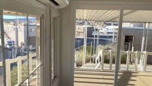 Una habitación con ventanas amplias, ventilador de techo y vista a un estacionamiento y edificios exteriores.