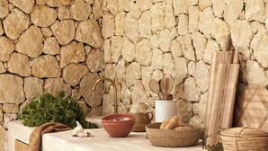 A rustic kitchen setting with a stone wall, wooden utensils, a bowl, and a basket of bread.