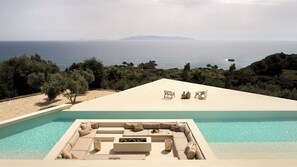 A poolside area with a seating arrangement and a view of the sea. - Sui Generis Villa (Argostoli)