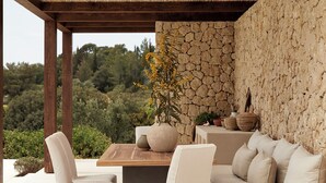 An outdoor seating area with a stone wall, wooden furniture, and a view of the surrounding landscape.