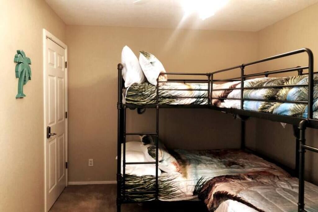A bunk bed with a patterned bedspread and pillows, a white door, and a small green plant on the wall.