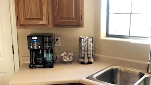 A kitchen with wooden cabinets, a coffee maker, a basket of coins, and a window with blinds. - The Gentleman's Jack, Moovalya Keys Value (Parker)