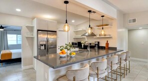Une cuisine moderne dotée d’un îlot central, d’appareils électroménagers en acier inoxydable et de luminaires suspendus.