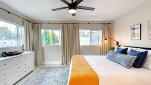Un dormitorio con cama, ventilador de techo, ventana con cortinas, cómoda y alfombra.