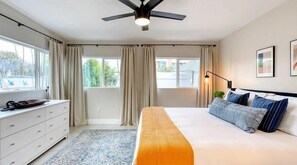 A bedroom with a bed, a ceiling fan, a window with curtains, a dresser, and a rug.