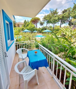 A balcony with a table and chairs, a pool, and surrounding greenery.