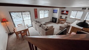 Una sala de estar acogedora con chimenea, comedor y ventanas amplias con vista a un paisaje nevado.