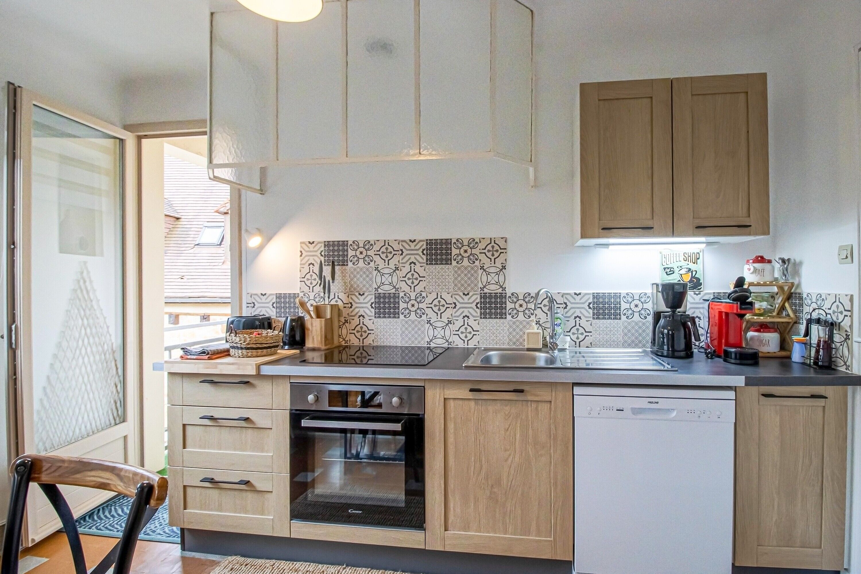 Eine moderne Küche mit Holzschränken, einem Geschirrspüler, einem Backofen und einer Kaffeemaschine.