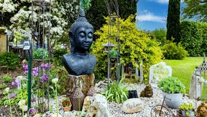 A garden with a Buddha statue, potted plants, rocks, and a bicycle.