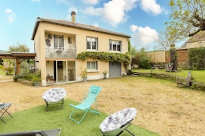 A two-story house with a balcony, a lawn, and two lounge chairs.