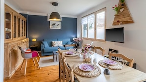 A dining area with a wooden table set for four, a blue sofa, a cabinet, and a wall-mounted TV.