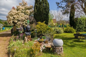 A garden with a statue, a tall tree, and a bench.