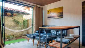A cozy room with a hammock, a dining table, and a view of a brick wall and greenery outside.