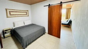 A bedroom with a bed, a nightstand, a wooden door, and a view into another room.