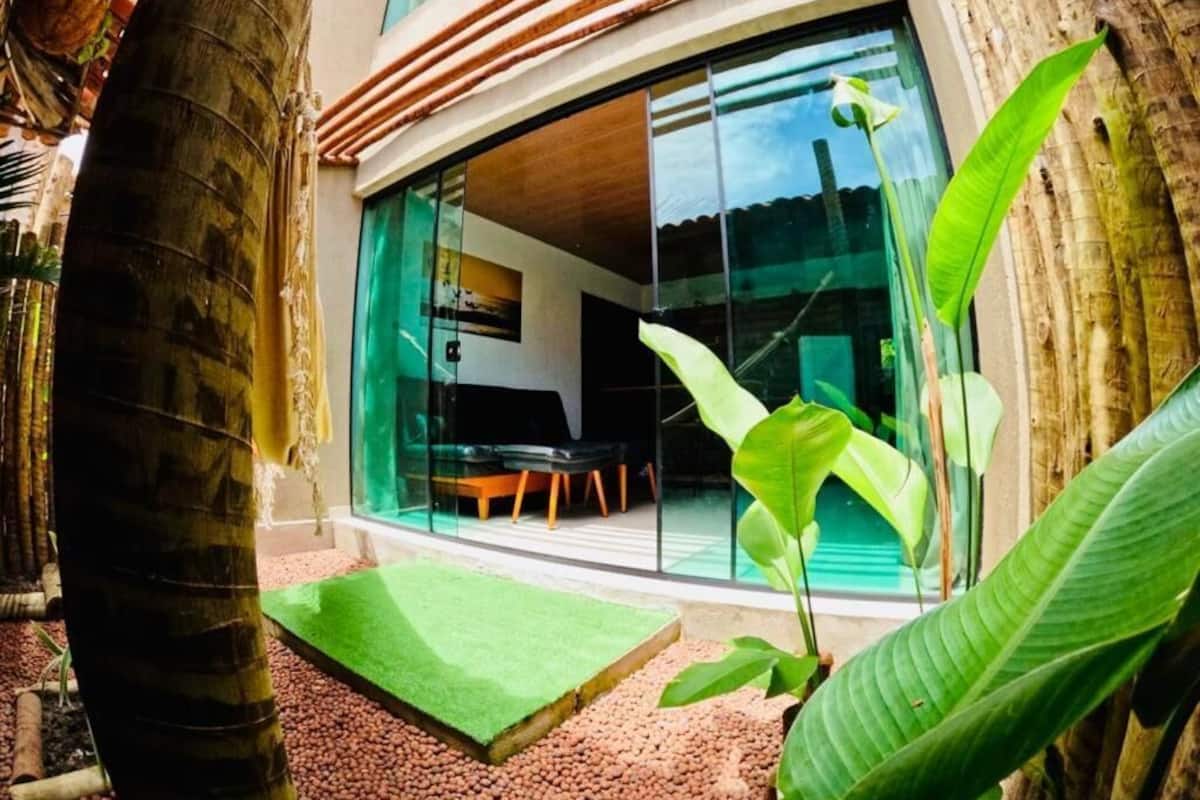 A modern building with large glass doors, a green outdoor area with a small table, and tropical plants.