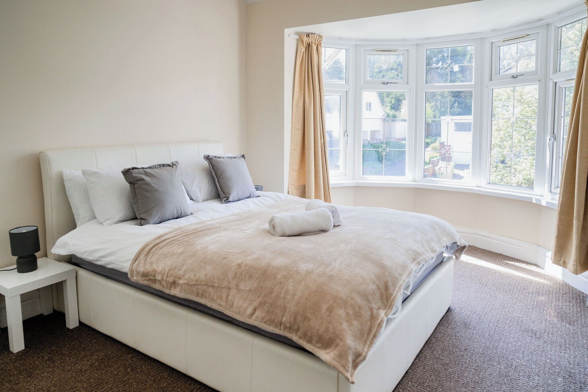 A bedroom with a large bed, a nightstand, and a window with curtains.