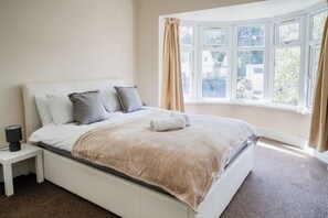 A bedroom with a large bed, a nightstand, and a window with curtains. - 6-bed House - Sleeps 13 - Families & Contractors (Dudley)