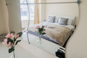Un dormitorio ordenado con cama, almohadas, un jarrón con flores y una mesita de noche.