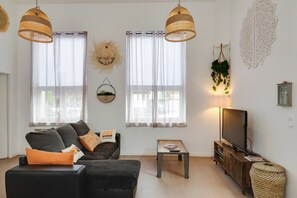 A living room with a sofa, ottoman, TV stand, and two hanging lamps.