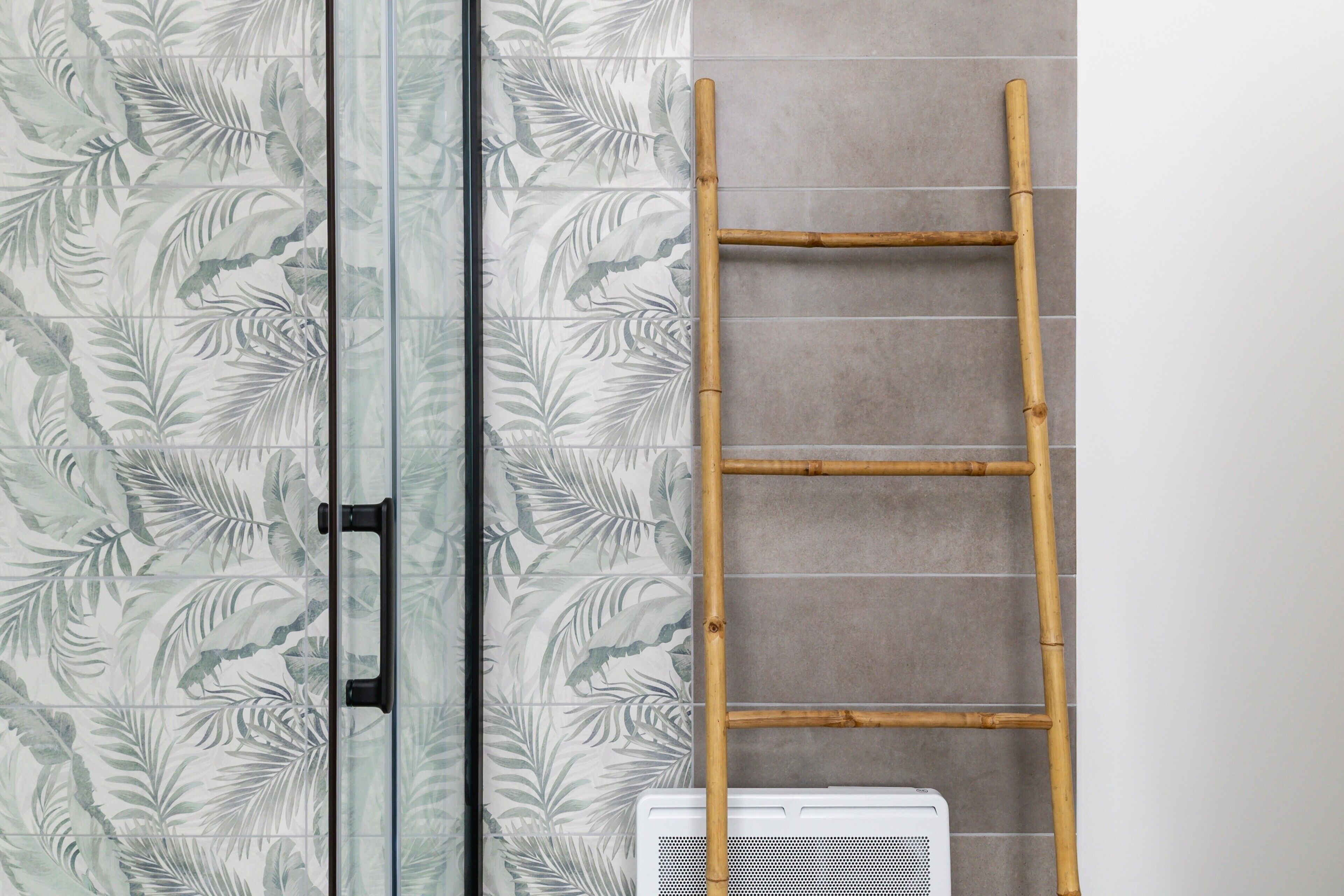Une salle de bain avec une porte de douche en verre, un escabeau en bambou et un radiateur blanc.