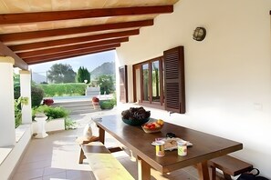 Un área de comedor al aire libre con una mesa de madera, un cuenco de frutas y una planta en maceta.