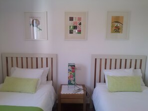 Habitación de hotel con dos camas, una mesita de noche y tres cuadros enmarcados en la pared.