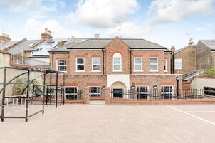 A two-story brick building with a central archway, large windows, and a paved courtyard.
