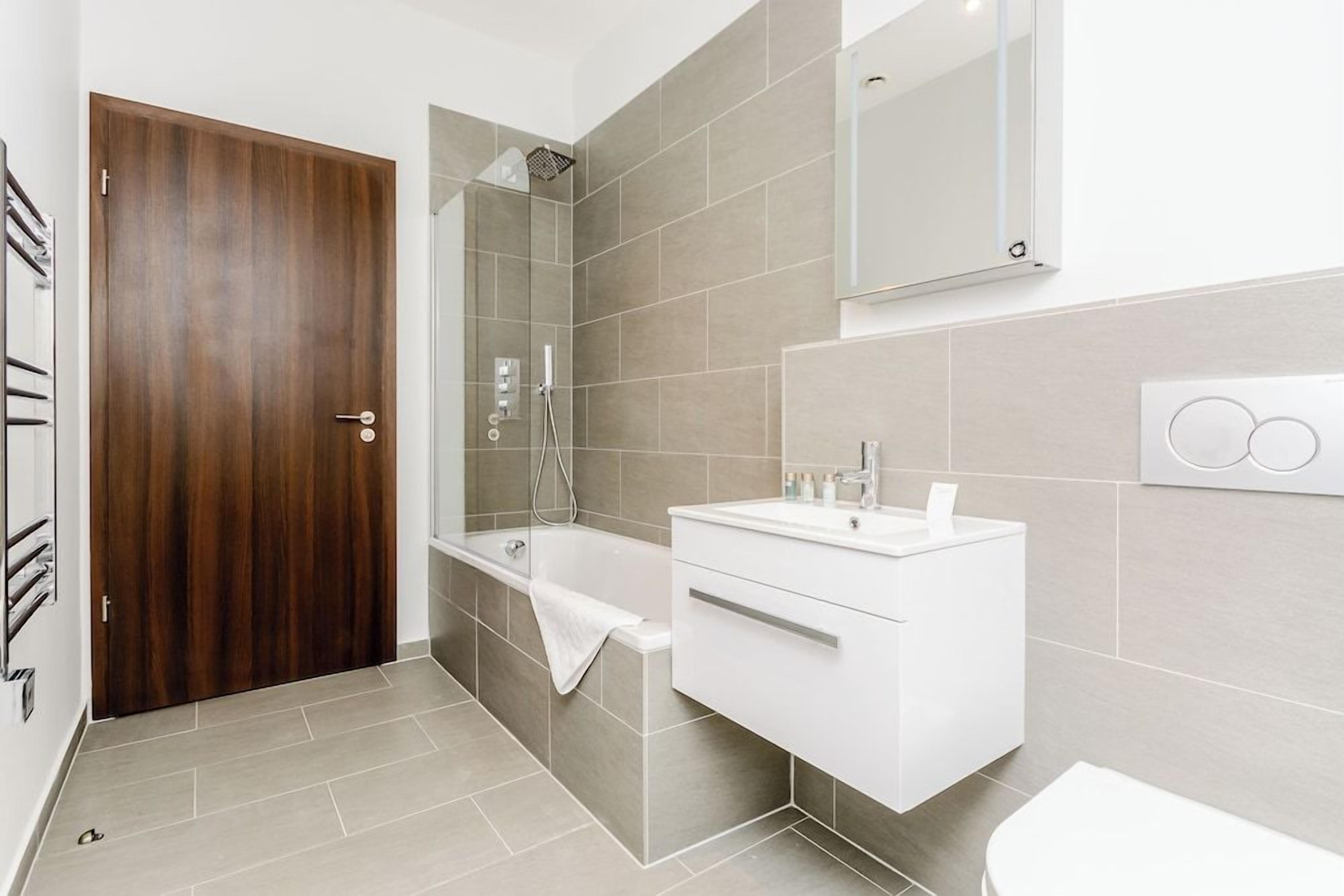 Un baño moderno con puerta de madera, bañera, ducha y tocador blanco.