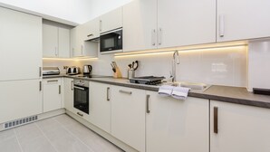 A modern kitchen with white cabinets, a built-in microwave, a stove, and a sink. - Flying Butler Richmond Tersha Street Apartments (Richmond)