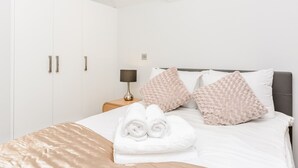 A neatly made bed with white linens, two fluffy pillows, and a set of towels. - Flying Butler Richmond Tersha Street Apartments (Richmond)