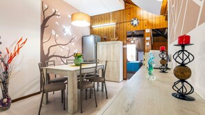 A dining area with a wooden table, chairs, a vase with flowers, and a wall with a tree design. - Apartment 'Reale' with Private Terrace, Wi-Fi and Air Conditioning (Gravina di Catania)