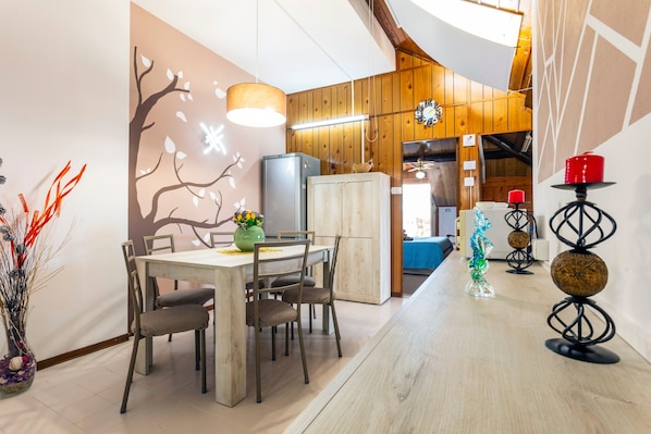 Un coin repas avec une table en bois, des chaises, un vase de fleurs et un mur décoré d’un motif d’arbre.